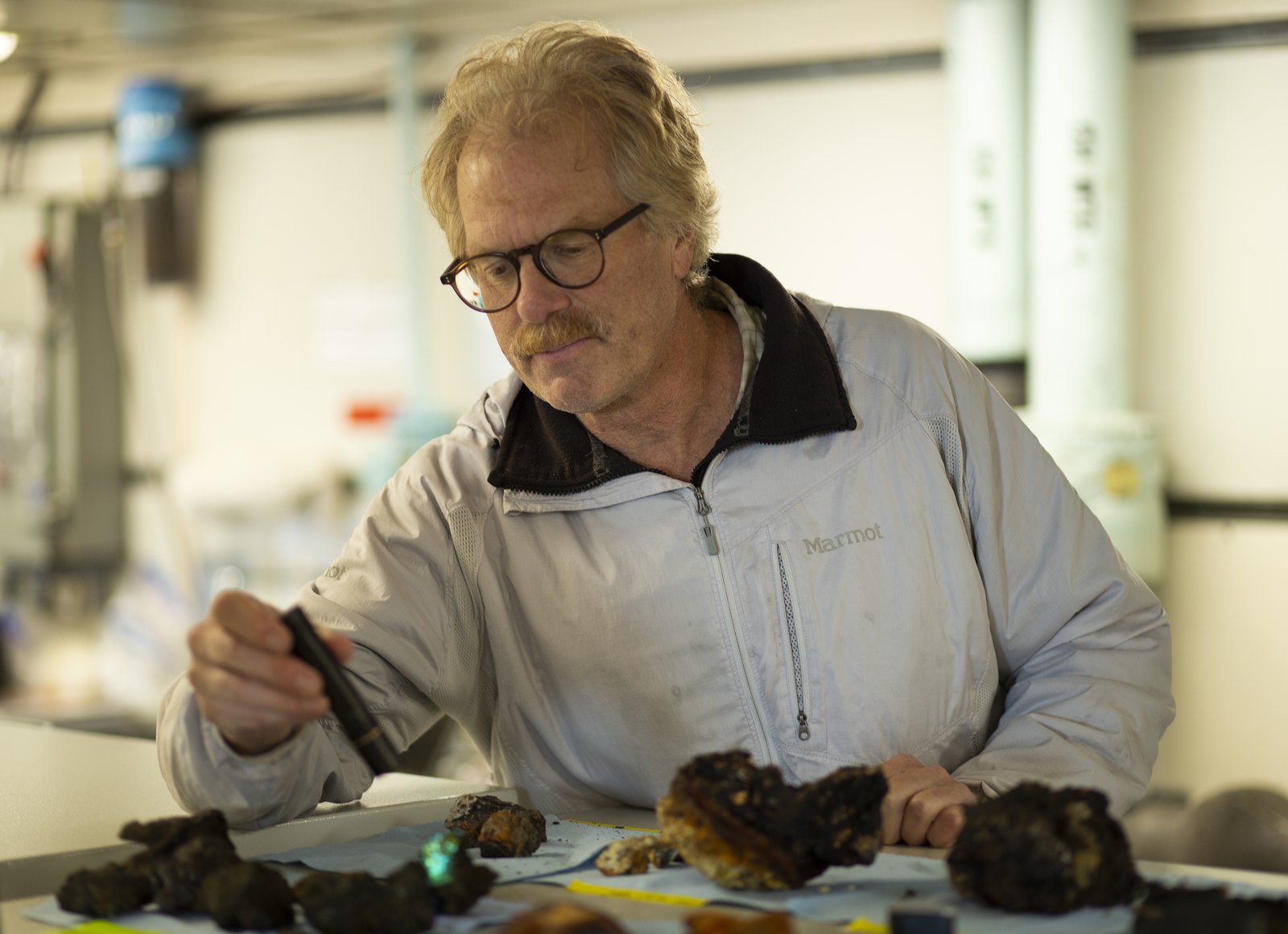 A man shines a small light on some rock samples.